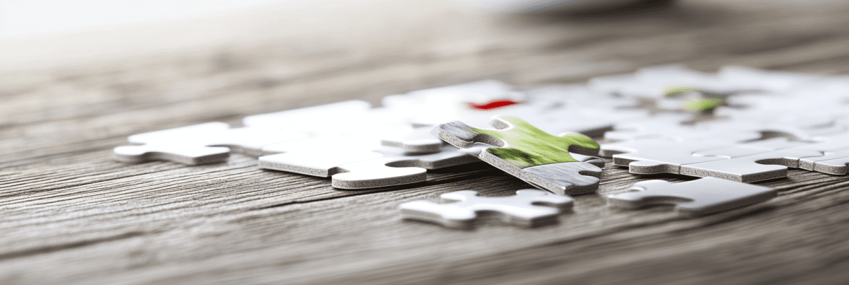A close-up of a partially completed jigsaw puzzle on a wooden table, with one colorful piece resting above its place, suggesting paused but meaningful creative progress.