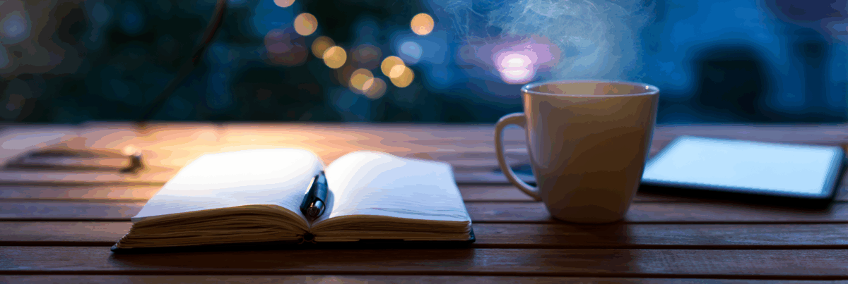 A warmly lit open notebook and a steaming mug sit on a wooden table at twilight, with blurred lights glowing softly in the background and a digital tablet resting nearby.