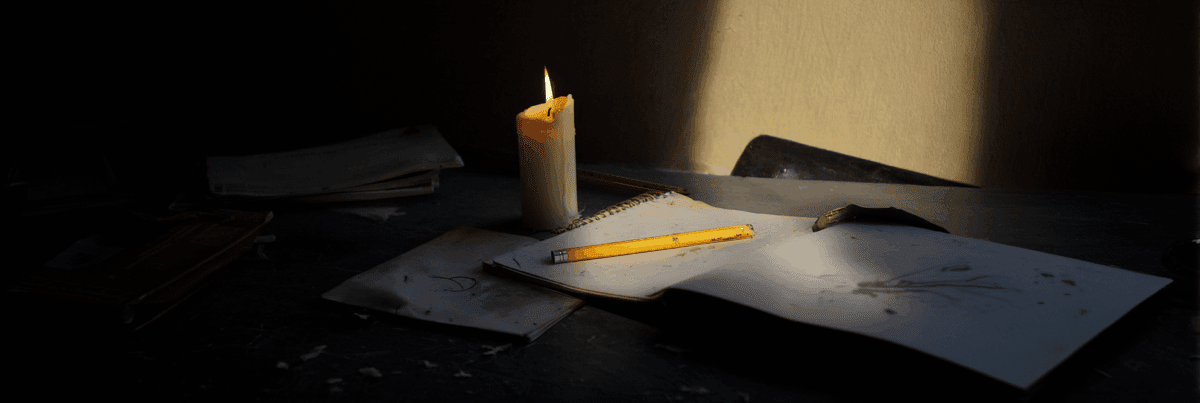 A dimly lit table with a single burning candle beside worn notebooks and a yellow pencil. Shadows stretch across the scene, suggesting a sense of quiet persistence and the fragile warmth of ideas that haven’t faded.