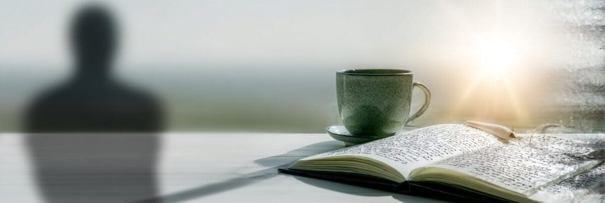An open journal filled with handwritten notes rests beside a green mug on a windowsill. Sunlight filters through a misted window, casting a faint human silhouette and creating a quiet, reflective mood.