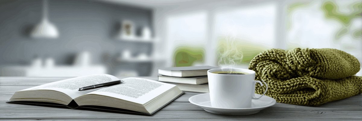 An open book and a steaming cup of coffee sit on a wooden table beside a folded green knitted blanket. Sunlight fills the softly blurred room, evoking warmth, comfort, and peaceful pause.