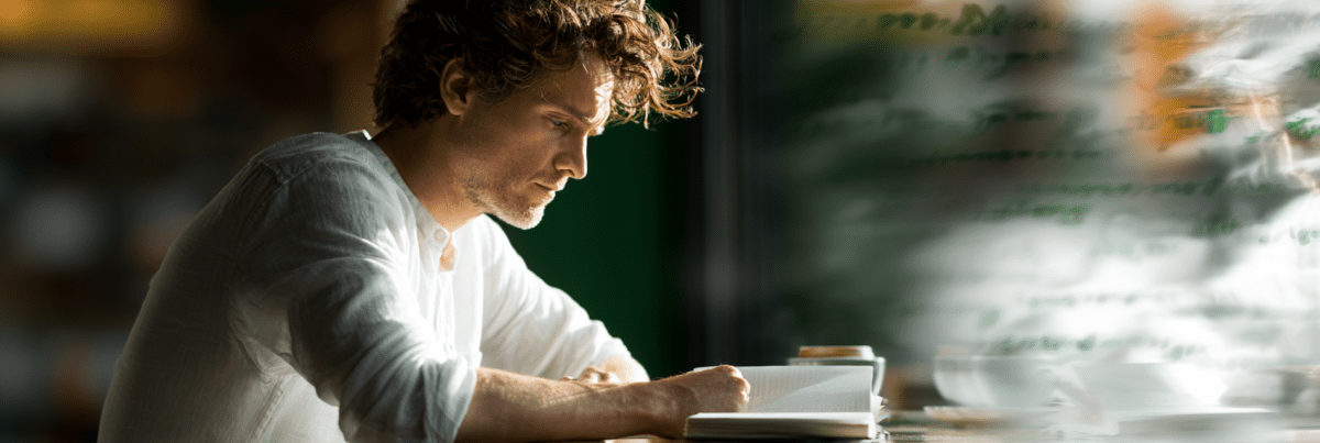 A thoughtful person reads at a café table beside a window while blurred text-like reflections and soft abstract shapes hover in the glass, evoking the subtle influence of invisible digital tools on daily thinking and learning.