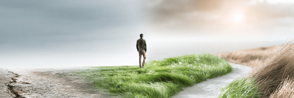 A solitary person pauses where a worn pale path meets a new green path stretching toward a bright, uncertain horizon.