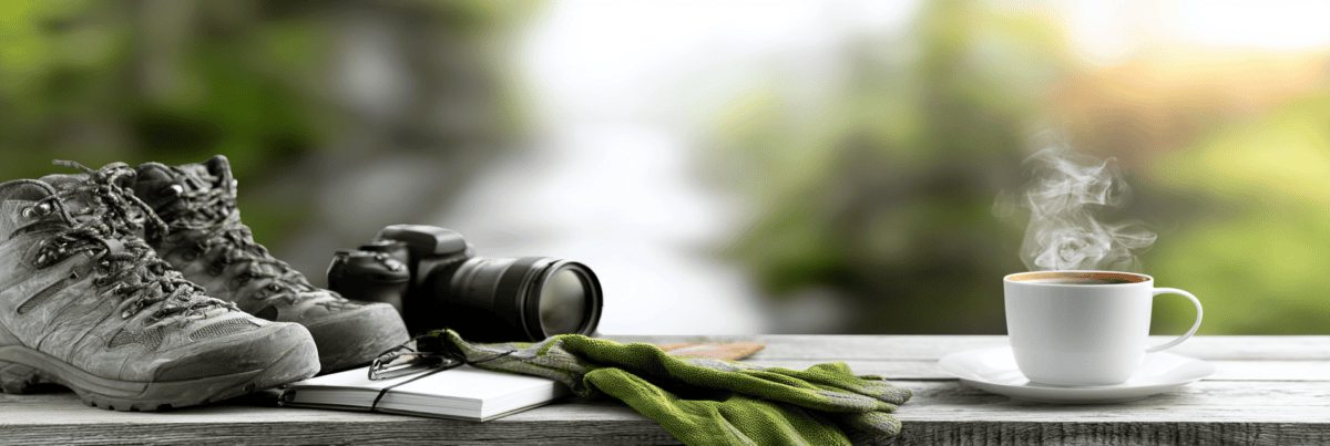 Well-worn hiking boots, a camera, gardening gloves, a notebook, reading glasses, and a steaming cup of coffee rest together on a wooden table, symbolizing that curiosity can continue to grow through many different interests at any stage of life.